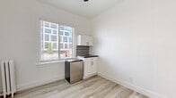 Located at 5849 Sunset Boulevard in the heart of Hollywood, Los Angeles, this compact one-bedroom, one-bathroom unit offers a efficiently designed single-floor layout. The main living area is finished with light wood-style laminate flooring and crisp white walls that lend a clean, bright aesthetic throughout. A window with horizontal blinds allows natural light to filter in while providing views of the surrounding urban streetscape. A vintage-style cast iron radiator adds a touch of classic character to the space.

The kitchenette is neatly integrated into the layout, featuring white cabinetry with modern hardware, a dark stone-style countertop, and a compact stainless steel refrigerator. The bedroom area is accessed through a white paneled door and includes a built-in open closet, offering practical storage solutions within the modest footprint.

The bathroom is finished with white square ceramic tile lining the walls of the tub surround, complemented by a small window that introduces natural light. The overall palette of the unit — white walls, light flooring, and minimal detailing — creates a cohesive and functional living environment well-suited to urban life in one of Los Angeles' most iconic neighborhoods.