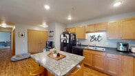 This single-floor residence offers a thoughtfully designed layout with warm, welcoming finishes throughout. The kitchen is a functional centerpiece, featuring honey-toned wood cabinetry, dark countertops, and a full suite of black appliances including a range, dishwasher, and refrigerator. A granite-topped island provides additional prep space and casual seating, while a dedicated coffee bar area adds a charming and practical touch. Wood-look flooring runs throughout the main living areas, lending warmth and continuity to the space.

The living room is generously sized and features a ceiling fan, a sliding glass door that fills the room with natural light and provides outdoor access, and a built-in entertainment area with an electric fireplace below the mounted television. The room comfortably accommodates multiple seating arrangements, creating an inviting atmosphere for relaxing or entertaining.

Two carpeted bedrooms offer restful retreats, each featuring ceiling fans and windows that bring in natural light. Both rooms are spacious enough to accommodate large bedroom furniture with ease. A flexible bonus room with carpet and a window serves well as a home office or additional sleeping space. The full bathroom includes a single-sink vanity with wood cabinetry, tile flooring, and a tub-shower combination.