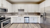 Located at 25 Station Ct in downtown Greenville, SC, this two-bedroom, two-bathroom single-floor residence offers a well-designed layout with a thoughtful blend of style and functionality. The open-concept kitchen and living area serves as the heart of the home, featuring durable hardwood-style flooring throughout. The kitchen is well-appointed with crisp white shaker cabinetry, grey subway tile backsplash, light quartz countertops, and stainless steel appliances including a refrigerator with ice maker, dishwasher, and range. The living area extends to a private balcony through a sliding glass door with vertical blinds, bringing in natural light and outdoor views. Both bedrooms are carpeted for comfort and equipped with ceiling fans. The generously sized primary bedroom includes a closet with wire shelving. A second bedroom features a dedicated closet and a window overlooking greenery. Each bathroom is finished with wood-style flooring, a white vanity with a framed mirror, and a full tub/shower combination with tile surround and brushed nickel fixtures. Two hallways connect the living and private areas seamlessly, complemented by neutral warm-toned walls throughout that lend the space a clean, welcoming ambiance.