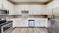 Located at 25 Station Ct in downtown Greenville, SC, this two-bedroom, two-bathroom single-floor residence offers a well-designed layout with a thoughtful blend of style and functionality. The open-concept kitchen and living area serves as the heart of the home, featuring durable hardwood-style flooring throughout. The kitchen is well-appointed with crisp white shaker cabinetry, grey subway tile backsplash, light quartz countertops, and stainless steel appliances including a refrigerator with ice maker, dishwasher, and range. The living area extends to a private balcony through a sliding glass door with vertical blinds, bringing in natural light and outdoor views. Both bedrooms are carpeted for comfort and equipped with ceiling fans. The generously sized primary bedroom includes a closet with wire shelving. A second bedroom features a dedicated closet and a window overlooking greenery. Each bathroom is finished with wood-style flooring, a white vanity with a framed mirror, and a full tub/shower combination with tile surround and brushed nickel fixtures. Two hallways connect the living and private areas seamlessly, complemented by neutral warm-toned walls throughout that lend the space a clean, welcoming ambiance.