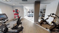 Located at 741 N Dearborn Street in Chicago's vibrant River North neighborhood, this fitness center offers a comprehensive, well-organized workout facility spread across a single floor. The space is designed to accommodate a wide range of exercise needs, with distinct zones dedicated to different types of training.

The cardio area is prominently featured, housing a row of treadmills with individual screens positioned alongside floor-to-ceiling windows that frame views of the surrounding cityscape, providing natural light and an energizing atmosphere. Additional cardio equipment includes multiple Life Cycle stationary bikes, Cybex elliptical trainers, and cross-trainers, offering users a full variety of low-impact and high-intensity options.

A dedicated studio space features mirrored walls, a wall-mounted flat-screen television, and a range of group fitness accessories including step platforms, stability balls, and hand weights on a rack — making it ideal for classes or individual training sessions. Ceiling fans are positioned throughout to maintain airflow and comfort.

The flooring consists of durable, patterned carpet tiles throughout the exercise areas, complemented by a drop-panel ceiling with recessed and overhead lighting. Multiple windows allow natural light to filter in across all zones. The overall aesthetic is clean, modern, and functional, reflecting a professional fitness environment well-suited to daily use.