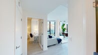 This single-floor residence showcases a contemporary design characterized by clean lines, crisp white walls, and light wood flooring throughout. The open-concept living area is anchored by dramatic floor-to-ceiling black-framed windows that flood the space with natural light and frame sweeping urban skyline views. A sectional sofa, glass coffee table, and bold abstract wall art contribute to the room's modern aesthetic.

The primary bedroom continues the bright, airy theme with expansive floor-to-ceiling windows offering city views, light wood flooring, and neutral tones that create a calm and restful atmosphere. A secondary bedroom provides a well-proportioned, cozy retreat with soft lighting and tasteful décor.

The hallways are clean and efficiently designed, connecting bedrooms and bathrooms with ease. Two bathrooms serve the residence: one features a full soaking tub with a tiled shower surround and chrome fixtures, while the second is a more compact water closet with tile flooring and framed wall art. Throughout, the design prioritizes a cohesive, minimalist palette, maximizing both functionality and the sense of open, light-filled urban living.