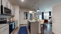This single-story, one-bedroom, one-bathroom residence is thoughtfully designed to maximize functionality and style throughout its well-proportioned layout. The open-concept kitchen serves as a central feature, showcasing gray shaker-style cabinetry, granite countertops, a mosaic tile backsplash, and a full suite of stainless steel appliances. A center island with seating for two is illuminated by a trio of polished pendant lights, creating a natural gathering point that flows seamlessly into the dining area. Wood-style flooring extends throughout the main living spaces, adding warmth and continuity.

The living room is bright and welcoming, featuring large windows with blinds and floor-length navy drapes that frame a glass patio door, bringing in natural light and providing outdoor access. A ceiling fan adds practical comfort to the space.

The bedroom is carpeted and generously sized, accommodating a large bed with ease. It includes a walk-in closet with built-in shelving, offering ample storage. A ceiling fan and soft neutral walls contribute to a restful atmosphere.

The bathroom features wood-style flooring, gray cabinetry with a vanity, and a shower-tub combination, maintaining the consistent modern aesthetic found throughout the residence.