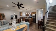 This 2-floor space presents a well-designed open-concept main level that seamlessly connects the living, dining, and kitchen areas. Dark hardwood flooring runs throughout, lending warmth and cohesion to the space. Crown molding adds a refined architectural touch to the ceilings, which are fitted with a ceiling fan for added comfort.

The kitchen is a functional centerpiece, featuring warm-toned cabinetry, dark granite countertops, and a full suite of stainless steel appliances, including a refrigerator, range, and built-in microwave. A kitchen island with bar seating provides an additional prep and dining surface, while pendant lighting above creates focused illumination. A stainless steel sink is positioned near a window, allowing natural light to filter in.

The adjacent living area accommodates comfortable seating and is anchored by a media console. The dining area, situated nearby, offers space for a full table and chair set. A hallway leads toward additional areas of the home, including access to the second floor. The overall layout is practical and inviting, balancing everyday functionality with a cohesive design aesthetic.