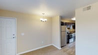 This single-floor space offers a practical and inviting layout, highlighted by a seamless transition between the dining area and kitchen. The dining area features neutral beige walls, light carpet flooring, and a modest chandelier that provides warm, ambient lighting — lending a welcoming atmosphere to the space. White baseboards offer a clean contrast against the neutral tones throughout.

The kitchen, partially open to the dining area, is outfitted with dark espresso-toned cabinetry that provides ample storage. Stainless steel appliances, including a refrigerator, gas range, and dishwasher, contribute a modern touch. A sink is positioned beneath upper cabinetry, and the kitchen features durable wood-look flooring that contrasts neatly with the carpeted dining space. Flush ceiling lighting ensures the kitchen remains well-lit and functional.

The open-concept connection between the two areas promotes a sense of flow, making the space feel cohesive and efficient. The overall aesthetic is clean and understated, combining practical finishes with a neutral palette suited to a variety of interior styles.