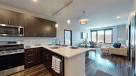 Located at 2000 Pennsylvania Ave in Wilmington, Delaware, this contemporary single-floor residence showcases a thoughtfully designed open-concept layout with modern finishes throughout. The kitchen is a standout feature, outfitted with rich dark wood cabinetry, stainless steel appliances, a white subway tile backsplash, light quartz countertops, and a central island with pendant lighting — all set atop warm hardwood flooring that extends into the living and dining areas. Track lighting and flush-mount fixtures provide ample illumination throughout the shared living space, which is framed by large black-framed windows offering expansive urban views and abundant natural light. The bedrooms are generously proportioned, each featuring sliding or casement windows that flood the rooms with daylight, ceiling fans, and hardwood or wood-look flooring. Two bathrooms serve the residence: one full bath with dark wood vanity cabinetry, a tub-shower combo with tiled surround, and large-format tile flooring, and a second bath finished with a sleek vanity and coordinating tile. The overall aesthetic is clean, modern, and cohesive, combining neutral tones with bold dark accents for a sophisticated urban feel.