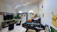 This single-floor game room is designed with entertainment and nostalgia in mind, making it an engaging retreat for players of all ages. The walls serve as a standout feature, adorned with colorful, hand-painted murals inspired by classic retro video games, including iconic characters, question-mark blocks, warp pipes, and mushrooms that bring a playful, immersive atmosphere to the space.

The room is equipped with a full-size foosball table positioned centrally, offering a focal point for competitive play. A custom arcade machine cabinet adds an authentic retro gaming experience, complementing the themed décor seamlessly. A sleek, ergonomic floor gaming chair provides a comfortable seating option for console or screen-based gaming.

Recessed ceiling lighting combined with modern wall sconces ensures the room is well-lit, creating a lively yet comfortable ambiance. The light-toned flooring contrasts with the vibrant wall art, keeping the space feeling open and energetic. Overall, this game room is thoughtfully curated to deliver an immersive, fun-filled environment centered entirely around gaming culture and entertainment.