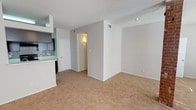 This single-floor residence offers a well-organized layout with distinct living, kitchen, bedroom, and bathroom areas. The spacious living room serves as the centerpiece of the home, featuring a classic brick fireplace flanked by two windows that bring in natural light. A ceiling fan adds comfort, and the room is finished with plush wall-to-wall carpeting and a textured ceiling.

The galley-style kitchen is both functional and stylish, outfitted with dark espresso cabinetry, light speckled countertops, and a mosaic tile backsplash. Black appliances, including an electric range and refrigerator, complement the design, while warm hardwood-style flooring ties the space together. The kitchen opens conveniently toward the main living and dining areas.

The bedroom is generously sized, carpeted, and includes a ceiling fan with a window providing natural light. A dedicated walk-in closet offers ample storage, and a separate doorway leads to additional hallway access.

The bathroom features dark cabinetry with a wide vanity, speckled countertops, a large mirror with overhead lighting, and hardwood-style flooring—providing a clean, practical finish. Throughout the home, neutral gray walls, consistent flooring transitions, and thoughtful detailing contribute to a cohesive and comfortable living environment.