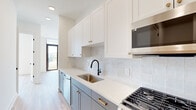 Located at 1015 Boulevard SE in Atlanta's vibrant Grant Park neighborhood, this modern single-floor residence showcases a clean, contemporary design throughout. The kitchen is a standout feature, combining white upper shaker cabinets with slate-blue lower cabinets, white quartz countertops, a white subway tile backsplash, and gold and matte black hardware accents. Stainless steel appliances — including a gas range, built-in microwave, and a full-size refrigerator — complete the space. A convenient in-unit stacked washer and dryer is tucked just off the kitchen. The bathroom features light wood-look flooring, a glass-enclosed walk-in shower, a gray vanity with gold hardware, and crisp white walls that create a clean, spa-like atmosphere. Living and sleeping areas are finished with the same warm wood-look flooring and bright white walls, offering a versatile, light-filled backdrop. Large floor-to-ceiling sliding glass doors and a full-lite exterior door connect the interior to outdoor spaces, flooding the unit with natural light and providing views of the surrounding greenery and community grounds. The overall aesthetic is modern and cohesive, with thoughtful finishes that balance style and functionality throughout.
