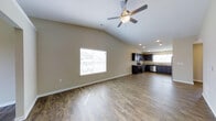 This single-floor residence offers an open-concept layout that combines the living and kitchen areas into one expansive, cohesive space. The living area is defined by dramatic vaulted ceilings that create an impressive sense of height and volume, complemented by a ceiling fan with integrated lighting that ensures year-round comfort. Smooth, neutral-toned walls provide a clean, versatile backdrop, while a large window floods the space with abundant natural light, enhancing the airy atmosphere.

The flooring throughout is a warm, wood-style hard surface that adds texture and continuity, seamlessly connecting the living and kitchen zones. Recessed lighting is thoughtfully placed in the kitchen area to ensure bright, even illumination for food preparation and entertaining.

The kitchen is well-appointed with rich, dark cabinetry that provides generous storage, paired with stainless steel appliances including a range and dishwasher. A sink is positioned beneath a window, offering natural light while completing daily tasks. The overall design balances functionality with contemporary style, making this home an inviting and practical living environment.