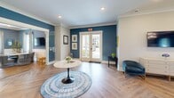 Located at 50 Newport Blvd in Port Wentworth, Georgia, this thoughtfully designed single-floor space offers a refined and professional atmosphere across a well-utilized footprint. The interior is defined by a cohesive coastal-inspired palette, with rich steel-blue accent walls contrasted by crisp white wainscoting and crown molding throughout.

The welcoming entry area features gleaming herringbone-pattern hardwood floors, a set of glass-paneled double doors that flood the space with natural light, and curated artwork that sets an inviting tone from the moment you arrive.

The main living area serves as a versatile workspace, accommodating multiple desks and seating arrangements beneath a striking gold-toned multi-globe chandelier. Large windows dressed with patterned drapery frame outdoor views and allow ample natural light to fill the room.

The dining room functions as a conference and meeting space, centered around a round wood table with upholstered chairs, a wall-mounted display screen, and additional gold-accented lighting overhead — ideal for collaborative gatherings.

The kitchen is compact yet efficiently appointed, featuring white shaker cabinetry, a soft blue subway tile backsplash, marble-look tile flooring, a stainless steel refrigerator, and a single basin sink — providing all essential amenities in a clean, stylish package. Together, these spaces create a cohesive, functional, and elegantly detailed environment.