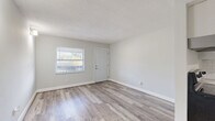 Located at 1279 Santa Rosa St in Clearwater, Florida, this single-story, one-bedroom, one-bathroom unit offers a well-organized and efficiently designed layout. Throughout the space, light-toned wood-look flooring creates a clean, cohesive aesthetic that ties each room together seamlessly.

The living room serves as the entry point to the unit, featuring a large window that invites ample natural light and offers views of the lush Florida landscape, including a visible palm tree. A wall-mounted light fixture adds a functional accent, while soft gray walls maintain a neutral, airy atmosphere. A textured ceiling adds subtle architectural detail.

The bedroom is a comfortable, well-proportioned room complete with a built-in closet featuring double panel doors for convenient storage. A dedicated utility connection area is also present within the room, and an additional hallway panel provides easy access to utility controls.

The bathroom showcases a refined finish with large-format marble-look wall tiles surrounding a clean white soaking tub, giving the space an elevated and polished feel. The muted gray and white palette carries throughout the unit, lending a modern yet understated character to the overall design.

The hallway connects the rooms efficiently, contributing to the home's practical and straightforward flow. This unit is ideal for those seeking a compact, well-appointed living space in Clearwater, FL.