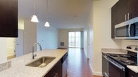This 2-bedroom, 2-bathroom residence offers a thoughtfully designed single-floor layout that balances comfort and functionality. The open-concept living area flows seamlessly from the kitchen through to the main living space, creating a bright and connected environment. The kitchen is outfitted with granite countertops, dark cabinetry, a stainless steel undermount sink with a pull-down faucet, and stainless steel appliances including a dishwasher and range. Pendant lighting above the kitchen island adds a stylish, modern touch. Hardwood flooring runs throughout the main living areas, lending warmth and cohesion to the space. The living area benefits from generous natural light streaming through large sliding glass doors, which provide access to an outdoor area and frame views of the surrounding environment. Soft, neutral wall tones create a calm and versatile backdrop throughout the home. The unit includes two well-proportioned bedrooms and two full bathrooms, offering practical layout options for residents. With its clean lines, quality finishes, and open design, this residence provides a comfortable and move-in-ready living experience.