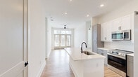 Located at 10410 Sam Furr Road in Huntersville, NC, this well-appointed 2-bedroom, 2-bathroom residence offers a thoughtfully designed single-level floor plan. The open-concept living area seamlessly connects the kitchen, dining, and living spaces, all finished with light wood-tone flooring and crisp white walls that create a bright, airy atmosphere. The kitchen is a standout feature, boasting two-tone cabinetry with white upper cabinets and gray lower cabinets, a large center island with a white quartz countertop and undermount sink, stainless steel appliances including a refrigerator, range, and microwave, and a classic white tile backsplash. The living room receives generous natural light through floor-to-ceiling French doors fitted with transom windows, and is equipped with a ceiling fan. A private balcony extends from the main living area. Both bedrooms are well-proportioned, featuring ceiling fans, wood flooring, and natural light. The primary bedroom connects to an en-suite bathroom with dual gray vanities, black matte fixtures, a walk-in glass shower, and access to a walk-in closet with wire shelving. The second bathroom offers similar upscale finishes. Additional highlights include a dedicated laundry area, utility room, and ample closet storage throughout.
