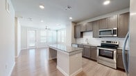 Located at 13003 FM-1488 in Magnolia, Texas, this single-story unit offers a thoughtfully designed open-concept layout with consistent wood-look flooring flowing throughout the space. The kitchen serves as a central highlight, featuring rich dark-brown cabinetry, granite countertops, a classic white subway tile backsplash, and a full suite of stainless steel appliances including a refrigerator, range, microwave, and dishwasher. A granite-topped center island provides additional workspace and casual seating. Recessed lighting illuminates the kitchen and transitions seamlessly into the adjacent living area, which benefits from multiple windows and a ceiling fan, filling the space with natural light and a sense of openness. The bedroom is a well-proportioned room with neutral tones, wood-look flooring, and direct access to a walk-in closet outfitted with wire shelving systems for organized storage. The bathroom includes a tiled soaking tub and shower combination with subway tile surround, a granite-topped vanity with dark cabinetry, and brushed nickel fixtures. Throughout the unit, clean white walls, recessed lighting, and consistent finishes create a cohesive, modern aesthetic.