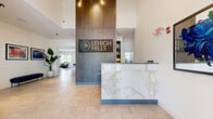 Located at 100 Aviv Street in Fogelsville, PA, this single-story community amenity center spans an expansive footprint across nine thoughtfully designed spaces, offering residents a comprehensive suite of lifestyle amenities. The interior opens to a welcoming lounge area featuring light hardwood flooring, a dramatic floor-to-ceiling marble-surround fireplace with a wall-mounted TV, built-in shelving, and generous natural light from oversized windows. The well-equipped fitness center houses a full array of strength machines and cardio equipment, including treadmills and ellipticals from True and Hoist, set against a striking textured accent wall with high ceilings and rubber flooring. An adjoining studio space provides hardwood floors, floor-to-ceiling mirrors, a ballet barre, and Stages spin cycles — ideal for group fitness classes. A vibrant children's play room features colorful geometric flooring, a whimsical mountain mural, and an assortment of play structures. Outdoors, a resort-style pool is flanked by a spacious stamped-concrete sundeck lined with lounge chairs, umbrellas, and a pergola structure. The grounds are further enhanced by meticulously maintained landscaping, featuring winding walking paths lined with ornamental trees, shrubs, and manicured greenery that create a tranquil, park-like setting throughout the community.