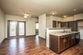 This single-floor unit offers a thoughtfully designed open-concept layout that seamlessly connects the living area and kitchen. Rich hardwood-style flooring flows throughout the main living spaces, adding warmth and continuity to the design. The living area is brightened by natural light pouring in through French doors that open to a private balcony, and is equipped with a ceiling fan for added comfort.

The kitchen features dark cabinetry with granite-style countertops, black appliances including a refrigerator, range, and microwave, and a peninsula with a built-in sink that doubles as a breakfast bar. A dedicated in-unit laundry room with a full-size washer and dryer is conveniently located just off the kitchen, along with additional utility storage.

Two generously sized bedrooms are finished with plush carpeting and each includes its own walk-in closet with built-in shelving. The bathrooms complement the overall design with dark wood vanities, granite-style countertops, and hardwood-style flooring. One bathroom features a full tub-shower combination, while the other functions as an en-suite. Dark-toned interior doors and bold baseboards throughout the unit create a cohesive, modern aesthetic.