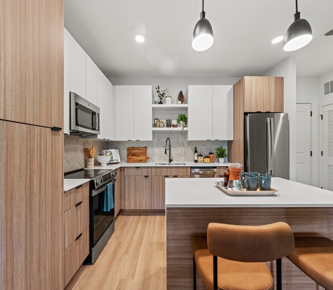 Cocina moderna con elegantes gabinetes de madera, elegante iluminación colgante y una acogedora isla de desayuno, perfecta para el entretenimiento. - Elan Crown Point