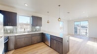 This thoughtfully designed single-floor residence offers a clean, contemporary aesthetic throughout. The kitchen serves as a standout centerpiece, featuring dark espresso cabinetry, a tiled backsplash, stone countertops, and a full suite of stainless steel appliances including a refrigerator, range, microwave, and dishwasher. A generous kitchen island with a stone surface provides additional prep and seating space, while pendant globe lights add a warm, modern touch. Multiple windows flood the kitchen and adjacent living area with natural light, creating a bright and inviting atmosphere. Light-toned hardwood-style flooring extends through the main living spaces, lending warmth and continuity to the open layout. The bedrooms are carpeted for comfort, with neutral tones and ample natural light from well-placed windows. At least one bedroom connects to a walk-in closet and an en-suite bathroom featuring a clean, white walk-in shower with brushed nickel fixtures. Sliding glass doors in one room offer outdoor access and additional natural light. Throughout the residence, recessed lighting, clean white walls, and modern hardware contribute to a cohesive and polished interior that balances practicality with contemporary style.