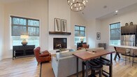Located at 3986 Parkmead Dr in Grove City, Ohio, this single-floor clubhouse is a well-appointed community gathering space designed with both comfort and functionality in mind. The open-concept layout is anchored by a dramatic vaulted ceiling that creates an airy, expansive atmosphere, complemented by light-toned hardwood flooring throughout.

The main lounge area serves as the heart of the space, featuring a floor-to-ceiling white brick fireplace with a dark wood mantel and a statement circular chandelier overhead. Comfortable seating arrangements, including plush sofas and leather accent chairs, invite relaxed conversation and socializing. Large gridded windows on multiple walls flood the interior with natural light and offer views of the surrounding neighborhood.

A dedicated recreation zone includes a full-size pool table and wall-mounted flat-screen televisions, providing entertainment options for residents. Additional casual seating areas are positioned near the oversized windows, creating bright, welcoming nooks ideal for lounging or informal gatherings.

The kitchenette is well-equipped with dark espresso cabinetry, stainless steel appliances including a full-size refrigerator, a single-basin sink, and light quartz countertops — offering convenient amenities for events and everyday use. A dining area with a warm wood table and seating rounds out the space, making this clubhouse a versatile and inviting hub for the community.
