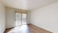 This single-story unit is designed with a clean, contemporary aesthetic throughout. The living area features wood-look flooring that extends through the main spaces, complemented by crisp white walls and a textured ceiling. A sliding glass door fitted with vertical blinds fills the room with natural light and provides direct access to an outdoor area, offering views of the surrounding greenery.

The kitchen is thoughtfully appointed with white cabinetry, quartz countertops, and a gray subway tile backsplash. A double stainless steel sink with brushed nickel fixtures sits beneath a window that brings in additional natural light. A dishwasher and electric range are also included, making the kitchen both functional and visually cohesive.

The bedroom features soft wall-to-wall carpeting and a window with vertical blinds, allowing for comfortable natural light control. The bathroom is well-equipped with a white vanity offering ample cabinet storage, a light bar above a large mirror, and wood-look flooring that ties the space together with the rest of the unit. Overall, the space maintains a bright, neutral palette throughout.