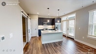 This single-story unit offers a thoughtfully designed layout across a compact yet efficient floor plan. The open-concept kitchen serves as the centerpiece of the living area, featuring navy blue shaker-style cabinetry extending to the ceiling, white quartz countertops, a full stainless steel appliance suite including a range, microwave, and French door refrigerator, and a central island with an undermount sink. Pendant lighting with an industrial aesthetic illuminates the island, while recessed lighting and large windows with outdoor views provide ample natural light throughout. A sliding barn door adds a contemporary architectural detail near the kitchen entry.

Hardwood-style flooring runs throughout the main living areas and hallway, while plush carpet covers the bedroom. The bedroom is a well-proportioned space with a ceiling fan, neutral wall tones, and direct access to a dedicated walk-in closet outfitted with built-in shelving and hanging rods. The bathroom continues the navy cabinetry theme with a shaker-style vanity, white quartz countertop, matte black fixtures, a framed mirror, and a sputnik-style light fixture, creating a cohesive, modern aesthetic throughout the unit.