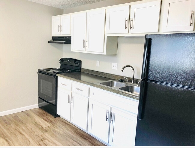 Modern kitchen with sleek black appliances, stylish white cabinetry, and elegant wood flooring. - Prentice Place