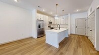 Located at 20 Graf Dairy Dr in Mobile, AL, this well-designed single-floor, one-bedroom, one-bathroom unit offers a clean, contemporary aesthetic throughout its efficiently utilized floor plan. The open-concept kitchen and living area serves as the heart of the home, anchored by a large white quartz-topped kitchen island with an undermount sink and matte black faucet. The kitchen is outfitted with crisp white flat-front cabinetry extending to the ceiling, a herringbone tile backsplash, stainless steel appliances including a French door refrigerator, electric range, and microwave, all illuminated by stylish brass pendant lights and recessed lighting. Wood-look flooring flows throughout the main living areas, lending warmth and continuity to the space. The living area benefits from natural light through a windowed exterior door. The bedroom features plush carpeting, a ceiling fan, and two windows that bring in ample natural light with outdoor views. The bathroom includes a wood-toned vanity with a white countertop, a glass-enclosed tiled shower, wood-look flooring, and direct access to a dedicated closet with built-in shelving. A separate laundry area completes the layout, adding functional convenience to this thoughtfully appointed home.