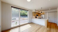 Located at 820 N State St in Bellingham, Washington, this modern one-bedroom, one-bathroom unit offers a thoughtfully designed layout with contemporary finishes throughout. The open-concept kitchen serves as the heart of the space, featuring flat-panel light wood cabinetry, a white quartz waterfall island with an undermount sink, stainless steel appliances including a French door refrigerator, electric range, and over-the-range microwave, all complemented by light hardwood-style flooring and pendant lighting overhead. The living and kitchen areas flow together seamlessly, creating an inviting, functional environment. The bedroom offers plush carpeted flooring and is bathed in natural light through a large floor-to-ceiling window with views of the surrounding Bellingham streetscape and skyline. A dedicated closet provides practical storage. The bathroom is cleanly appointed with a wood-toned vanity, matte black fixtures, a tub-shower combination, and matching hardwood-style flooring that ties the space together. Clean white walls and recessed lighting throughout the unit contribute to a bright, modern ambiance. This well-appointed unit combines efficient use of space with quality materials, making it an attractive option in the heart of Bellingham.