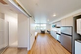 Located on University Way NE in Seattle's vibrant University District, this efficiently designed studio unit makes smart use of its compact footprint across a single floor. The open-plan layout seamlessly combines the living, dining, and kitchen areas into one cohesive space, maximizing functionality without sacrificing comfort. Light wood laminate flooring runs throughout the main area, lending warmth and visual continuity to the clean, modern interior. The kitchen is equipped with stainless steel appliances, including a full-size refrigerator, dishwasher, and microwave, complemented by gray cabinetry and a single-basin sink. A sliding barn door adds a contemporary architectural touch, separating the sleeping area from the main living space while conserving floor area. The sleeping area accommodates a platform bed and benefits from a large window that fills the room with natural light and offers neighborhood views. A dedicated dining nook with a small table and chairs provides a functional workspace and meal area. The bathroom features a glass-enclosed walk-in shower, a vanity with white cabinetry, and neutral flooring. An in-unit closet with hanging storage adds practical convenience. A wall-mounted mini-split system ensures year-round climate control. The overall design is minimal and modern, with white walls and recessed lighting creating a bright, clean ambiance throughout.