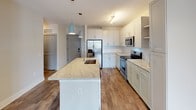 Located at 1315 Harding Pl in Charlotte's 28204 zip code, this single-floor unit offers a thoughtfully designed open-concept layout with clean, contemporary finishes throughout. The kitchen serves as the heart of the space, showcasing white shaker-style cabinetry, granite countertops, and a large center island with an undermount sink and stylish pendant lighting. Stainless steel appliances — including a refrigerator with ice maker, electric range, and built-in microwave — complete the well-appointed cooking area, which flows seamlessly into the main living space. Wood-look flooring extends through the main living and kitchen areas, adding warmth and continuity, while the bedroom features plush carpeting for added comfort. A dedicated built-in shelving unit in the bedroom area provides practical display and storage space. The bathroom is bright and functional, featuring light wood-tone tile flooring, a tub-shower combo, a vanity with dark granite countertop, and built-in wall shelving for organized storage. Neutral tones, recessed lighting, and a clean, modern aesthetic are consistent throughout, creating a cohesive and welcoming atmosphere ideal for comfortable everyday living.
