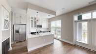 Located at 500 W Trade St in the heart of Charlotte, NC, this well-appointed 2-bedroom, 3-bathroom residence offers a thoughtfully designed single-floor layout. The open-concept kitchen is a standout feature, showcasing white shaker-style cabinetry with glass-front accents, dark lower cabinets, stainless steel appliances including a refrigerator, range, and built-in microwave, and a large center island with a white quartz countertop and undermount sink, finished with copper-toned pendant lighting. The kitchen flows naturally into the living area, which is bathed in natural light from expansive floor-to-ceiling windows and sliding glass doors that open to a private balcony overlooking the surrounding cityscape and greenery. Wood-look flooring runs consistently throughout, adding warmth to the neutral palette. The primary bedroom is generously sized, featuring a ceiling fan, interior glass partition windows, and access to a well-organized walk-in closet with built-in shelving and hanging rods. A second bedroom also includes its own closet. The three bathrooms are finished with tiled shower and tub surrounds. Two hallways provide smooth circulation throughout, and ample closet storage adds practical convenience to this modern urban residence.