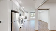 This well-appointed 1-bedroom, 1-bathroom unit offers a thoughtfully designed single-floor layout with a clean, contemporary aesthetic throughout. The open-concept kitchen and living area serves as the heart of the unit, featuring sleek white cabinetry extending to the ceiling, stainless steel appliances including a refrigerator, electric range, built-in microwave, and dishwasher, complemented by light countertops and a single-basin sink. Recessed lighting illuminates the space, while warm wood-look flooring flows seamlessly through every room, adding a sense of continuity and warmth.

The living area is bright and airy, with large floor-to-ceiling windows that invite abundant natural light and provide views of the surrounding neighborhood and greenery. The bedroom offers a comfortable and serene retreat, also benefiting from natural light through a well-placed window and featuring a dedicated closet space. The hallways connect the rooms efficiently, contributing to the unit's functional flow.

The bathroom is finished with marble-style tile in the tub/shower surround, pairing well with the clean white walls. An in-unit laundry area with a stacked washer and dryer adds everyday convenience. The overall ambiance is modern, bright, and move-in ready.