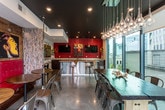 Located in Atlanta, GA 30326, this stylish single-floor lounge and entertainment space combines bold design elements with functional amenities. The open layout is anchored by a full kitchenette featuring rich dark wood cabinetry, stone countertops, a stainless steel sink, microwave, dishwasher, and a beverage cooler — all set against a striking glossy red geometric tile backsplash that serves as a dramatic focal point. Dual mounted flat-screen TVs flank vibrant artwork, adding to the lively atmosphere.

The lounge area is lined with reclaimed whitewashed wood-paneled walls that provide a rustic contrast to the bold color palette. Eclectic artwork throughout — including vivid paintings of jazz musicians and wine bottles — gives the space a gallery-like energy. Seating options are varied and inviting, from tufted red booth seating and bistro-style tables to modern bar stools and a communal dining table with industrial metal chairs.

A glass-walled dining nook at one end of the space is bathed in natural light, featuring floor-to-ceiling windows and glass doors that open directly to an outdoor terrace. A cascading glass pendant light installation adds an elegant touch overhead. Polished concrete flooring ties the entire space together, lending an urban, contemporary feel throughout.