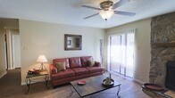 This single-story space in Texarkana offers a welcoming and functional layout designed for comfortable everyday living. The living area serves as the heart of the space, showcasing warm wood-style flooring that adds a sense of richness and continuity throughout the room. A textured ceiling with a ceiling fan and integrated light fixture provides both practical air circulation and ambient lighting, enhancing the room's overall comfort.

Natural light flows generously into the living area through a full-height sliding glass door fitted with vertical blinds, which offers both privacy control and easy access to an outdoor balcony. The slider frames views of the exterior, adding an open, airy quality to the interior. The neutral wall tones create a versatile backdrop that complements a range of furnishings and décor styles.

A decorative wall mirror with a rustic wood frame adds visual depth to the space, while the overall layout feels thoughtfully proportioned—cozy without feeling confined. The combination of natural light, durable flooring, and practical ceiling fixtures gives this space a grounded, livable ambiance well-suited for daily use.