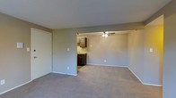 Located at 5051 Open Meadow Dr in Columbus, Ohio, this single-floor residence offers a straightforward and functional layout designed for comfortable everyday living. The main living area is generously sized, featuring neutral-toned carpet flooring and clean, smooth walls painted in a soft greige hue that creates a calm and understated ambiance throughout. A closet with a sliding door provides convenient storage directly off the living space. The living area flows openly into a dining or secondary living zone, distinguished by a ceiling fan that ensures year-round comfort and air circulation. Just beyond, the kitchen is partially open to the main living space, offering dark espresso-toned cabinetry paired with a light countertop. The kitchen includes a sink and upper and lower cabinet storage, making efficient use of the available space. Neutral-toned base trim runs consistently throughout, tying the rooms together cohesively. The overall design is clean and move-in ready, with a simple, practical aesthetic suited to a wide range of lifestyles. The single-floor layout ensures easy accessibility and seamless navigation between all areas of the home.