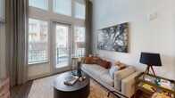 Located at 3750 Philemon Ave. in Charlotte, NC, this single-floor residence offers a thoughtfully designed layout with soaring ceilings that lend a sense of spaciousness throughout. The open-concept kitchen is a functional centerpiece, outfitted with white shaker cabinetry, granite countertops, a subway tile backsplash, and stainless steel appliances including a refrigerator, microwave, and range. A large kitchen island with seating provides an ideal space for casual dining, while hardwood-style flooring ties the area together seamlessly. The living room is bright and airy, featuring floor-to-ceiling windows and glass doors that open to a private balcony, allowing generous natural light and outdoor views. The primary bedroom enjoys tall ceilings, plush carpeting, and large windows overlooking the exterior. Its en-suite bathroom includes a dual-sink vanity with granite countertops, white cabinetry, and a shower-tub combination. A second bedroom offers generous proportions with similar high ceilings and comfortable carpeting, ideal as a guest room or home office. The second bathroom mirrors the refined finishes of the primary bath, featuring a single-sink granite vanity and a walk-in shower. Clean white walls, consistent finishes, and an abundance of natural light create a cohesive, modern ambiance throughout this well-appointed Charlotte residence.