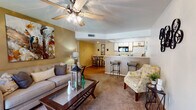 Located at 4700 N Kolb Rd in Tucson, Arizona, this single-story residence offers a well-organized layout designed for comfortable everyday living. The open-concept living area is warm and inviting, featuring warm golden-toned walls, plush carpeting, and a ceiling fan overhead. Natural light filters in through a sliding glass door that opens to an outdoor patio, creating a bright and airy atmosphere. The living space flows seamlessly into a dining area and kitchen, which is separated by a raised breakfast bar with barstool seating — ideal for casual dining or entertaining. The kitchen itself is efficiently designed with wood-accented cabinetry, light countertops, a full suite of appliances including a range, microwave, refrigerator, and a stainless steel sink, all set on durable wood-look flooring. The bedroom is a restful retreat, featuring vaulted-style ceilings, ceiling fan, plush carpeting, and a window with exterior views that allows natural light to brighten the room. The bathroom is clean and functional, offering a wide vanity with ample under-counter storage, a large mirror, and wood-look flooring. Throughout the space, consistent warm tones and thoughtful details create a cohesive and comfortable living environment.