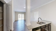 Located at 593 University Blvd in Round Rock, TX, this well-appointed one-bedroom, one-bathroom residence offers a thoughtfully organized single-floor layout. The open-concept kitchen flows seamlessly into the living area, featuring striking granite countertops, rich dark cabinetry with a mosaic tile backsplash, stainless steel appliances, and a built-in pantry with wire shelving for ample storage. Crown molding and hardwood-style flooring carry through the kitchen and living spaces, adding a polished, cohesive feel throughout. A decorative column defines the transition between the kitchen and the spacious living room, which is bathed in natural light from a large sliding glass door that opens to an outdoor view. The bedroom offers plush carpeting, a ceiling fan, and a natural light-filled window, creating a comfortable and restful retreat. An adjacent walk-in closet provides generous storage with multi-level wire shelving. The bathroom is finished with matching granite vanity countertops, dark cabinetry, neutral tile flooring, and a full bathtub-shower combination. Neutral tones and clean lines throughout give the space a bright, move-in-ready appeal well suited for comfortable everyday living.