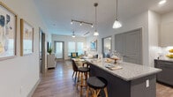This well-appointed single-floor residence offers a thoughtfully designed open-concept layout that seamlessly connects the kitchen, dining, and living areas. The kitchen is a standout feature, showcasing two-tone gray cabinetry, granite countertops, a large island with pendant lighting and barstool seating, stainless steel appliances, and a classic subway tile backsplash. Wood-style flooring flows throughout the main living areas, complemented by track lighting and ceiling fans that enhance both functionality and ambiance. The living room is bright and welcoming, with multiple windows that invite natural light and provide access to an outdoor balcony. Multiple bedrooms are carpeted for comfort, each offering generous closet space — including walk-in configurations — and large windows. The primary bedroom suite connects to a spacious bathroom featuring a dual-sink vanity with granite countertops, wood-style flooring, and a walk-in closet. Additional bathrooms maintain the same refined aesthetic with granite counters and gray cabinetry. Throughout the residence, a consistent neutral color palette punctuated by modern fixtures and contemporary décor creates a cohesive, upscale atmosphere suited for comfortable everyday living.