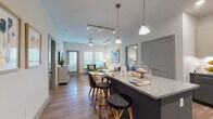 This well-appointed single-floor residence offers a thoughtfully designed open-concept layout that seamlessly connects the kitchen, dining, and living areas. The kitchen is a standout feature, showcasing two-tone gray cabinetry, granite countertops, a large island with pendant lighting and barstool seating, stainless steel appliances, and a classic subway tile backsplash. Wood-style flooring flows throughout the main living areas, complemented by track lighting and ceiling fans that enhance both functionality and ambiance. The living room is bright and welcoming, with multiple windows that invite natural light and provide access to an outdoor balcony. Multiple bedrooms are carpeted for comfort, each offering generous closet space — including walk-in configurations — and large windows. The primary bedroom suite connects to a spacious bathroom featuring a dual-sink vanity with granite countertops, wood-style flooring, and a walk-in closet. Additional bathrooms maintain the same refined aesthetic with granite counters and gray cabinetry. Throughout the residence, a consistent neutral color palette punctuated by modern fixtures and contemporary décor creates a cohesive, upscale atmosphere suited for comfortable everyday living.
