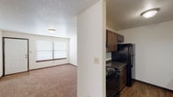 Located at 9211 E Harry St in Wichita, Kansas, this single-floor unit offers a practical and functional layout designed for comfortable everyday living. The galley-style kitchen is well-appointed with rich dark wood cabinetry, granite-toned countertops, wood-look flooring, and a full suite of black appliances including a refrigerator, electric range, and dishwasher. Ample upper and lower cabinet storage lines both sides of the kitchen, maximizing efficiency in the space.

The living area features neutral-toned carpeting, a textured ceiling, and a wide window fitted with horizontal blinds that allows natural light to filter in. The bedrooms continue the carpeted flooring and each include a ceiling fan with integrated lighting, providing both comfort and air circulation. Windows in the bedrooms offer additional natural light.

The unit includes two bathrooms. One features a vanity with a dark wood cabinet base, a countertop sink, a large mirror, and an adjoining room with a toilet and tub/shower combo. The second bathroom similarly features a clean white tub/shower surround with built-in shelving niches and a wall-mounted mirror. Wood-look flooring carries through the bathroom spaces, adding a cohesive design element throughout the unit.