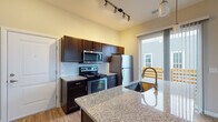 Located at 291 Graceland Blvd in Columbus, Ohio, this well-appointed single-floor residence offers a thoughtfully designed layout with modern finishes throughout. The kitchen serves as a central highlight, featuring rich dark-toned cabinetry, granite countertops, a large undermount sink, and a full suite of stainless steel appliances including a range, over-the-range microwave, and refrigerator. A subway tile backsplash adds a clean, contemporary touch, while track lighting illuminates the space effectively. A spacious island with matching granite provides additional prep and dining space. A sliding glass door leads directly from the kitchen to a private outdoor balcony, filling the area with natural light and offering convenient outdoor access. The bedroom is a comfortable, carpeted room with neutral tones and a window that brings in soft natural light. The bathroom is finished with wood-look flooring, a single vanity with a light countertop and dark cabinetry, and a large mirror. A doorway from the bathroom opens directly into a dedicated walk-in closet outfitted with built-in shelving and hanging rods, offering generous storage. Light wood-look flooring flows through the main living areas, complementing the warm, neutral color palette present throughout the home.