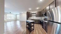 Located at 2183 S Withers Rd in Liberty, Missouri, this single-floor residence offers a thoughtfully designed open-concept layout accommodating two bedrooms and two full bathrooms. The kitchen is a standout feature, outfitted with rich dark espresso cabinetry, granite-look countertops, stainless steel appliances including a refrigerator, electric range, and over-the-range microwave, and a portable island that adds both prep space and versatility. Warm wood-style luxury vinyl plank flooring flows seamlessly from the kitchen into the spacious living room, which benefits from abundant natural light through large windows and is finished with a ceiling fan overhead. The primary bedroom offers a comfortable footprint with plush carpeting and direct access to a dedicated walk-in closet. The second bedroom is equally well-sized, also featuring soft carpet flooring and easy access to the hallway. The bathrooms continue the design theme with dark vanity cabinetry, granite-look countertops, and wood-style flooring. One bathroom features a walk-in shower with built-in shelving. Neutral wall tones, recessed lighting, and clean white trim tie the entire space together, creating a bright and cohesive living environment throughout.