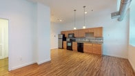This two-floor residence offers a well-designed layout with a thoughtful mix of materials and finishes throughout. The kitchen serves as a functional centerpiece, featuring warm honey-toned cabinetry, granite countertops with a tile backsplash, and a full suite of black appliances including a range, microwave, dishwasher, and stainless steel refrigerator. Pendant lighting above the kitchen area adds a polished touch, while durable hardwood-style flooring flows throughout the main living areas, lending warmth and cohesion to the space.

The bedrooms are carpeted for comfort and benefit from generous large-pane windows that invite natural light and offer views of the surrounding area. Exposed ductwork in select areas contributes an industrial character consistent with the building's architectural style.

Two bathrooms serve the residence, each finished with warm wood-toned vanities and clean white countertops. One bathroom features grab bars and a spacious, accessible layout, while the other includes a mirrored medicine cabinet with overhead vanity lighting.

A dedicated laundry closet houses a stacked Electrolux washer and dryer, providing in-unit convenience. Recessed lighting and crisp white walls throughout maintain a bright, clean aesthetic across both floors.
