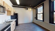 Located in the heart of downtown Spokane at 107 South Howard Street, Unit 406 is a thoughtfully designed urban residence that blends industrial character with modern finishes. The space features durable wood-style flooring throughout and striking dark-painted exposed ceilings with visible ductwork, lending an authentic loft aesthetic.

The open kitchen is outfitted with light maple cabinetry, a classic white tile backsplash, and a full suite of stainless steel appliances, including a refrigerator, electric range, built-in microwave, and dishwasher. The kitchen flows naturally into the main living area, which is bathed in natural light through large, black-framed windows offering views of the surrounding downtown Spokane skyline. A wall-mounted electric fireplace serves as a focal point in the living space, adding warmth and character.

The bathroom features a full tub-shower combination, a light wood vanity with an integrated sink, and clean white finishes accented by recessed lighting and bold black panel doors. A dedicated utility closet houses a stacked washer and dryer, providing the convenience of in-unit laundry. An entry hallway with a closet offers practical storage. The overall ambiance is modern and urban, ideal for those seeking a dynamic downtown Spokane lifestyle.