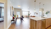This single-floor residence offers a thoughtfully designed open-concept layout that seamlessly connects the kitchen, dining, and living areas. The kitchen is a standout feature, equipped with stainless steel appliances including a range, microwave, and French door refrigerator, complemented by wood-toned cabinetry, white quartz countertops, a subway tile backsplash, and pendant lighting above a generous breakfast bar with seating. Light wood-style flooring flows throughout the main living areas, enhancing the bright, airy atmosphere created by recessed lighting and natural light from multiple windows. The dining area accommodates a full-sized table and connects directly to the living room, which features warm neutral tones and ample space for comfortable seating. Two well-proportioned bedrooms are finished with plush carpeting and large windows that invite natural light. Both bathrooms are finished with wood-tone vanities, white quartz countertops, and tub-shower combinations with white subway tile surrounds. The primary bathroom includes a dual-sink vanity and hardwood-style flooring. The overall design is cohesive and contemporary, blending warm wood tones with crisp white finishes throughout.