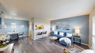 This charming 700 square foot home in Clute, Texas offers a thoughtfully designed living space with two bedrooms and one bathroom. The single-floor layout maximizes efficiency and flow. Upon entering, you're greeted by a light-filled living area featuring a blue accent wall and contemporary furnishings, creating a welcoming coastal ambiance.

The dining area showcases a stylish round table with seating for four, illuminated by a modern chandelier. A cohesive color scheme of soft blues and grays runs throughout the home, complemented by wood-look flooring that adds warmth and durability.

The primary bedroom, measuring 150 square feet, offers ample space and natural light through large windows. Both bedrooms feature neutral tones and plush bedding, providing comfortable retreats. The bathroom boasts a clean, modern design with a vanity and floral shower curtain.

The home's open concept encourages a sense of spaciousness, while thoughtful decor elements like coastal artwork and plants add character. Strategic lighting and mirrors enhance the perception of space. Despite its compact size, this home efficiently incorporates all essential living areas, including a hallway and closet space, making it an ideal option for those seeking a cozy yet functional living environment.
