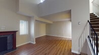 This two-floor space is defined by its striking architectural design, most notably the soaring vaulted ceilings that dramatically amplify the sense of openness in the main living area. Warm-toned hardwood-style flooring extends throughout the lower level, lending continuity and a polished feel to the space. The living room serves as a central focal point, anchored by a classic wood-burning fireplace framed by a dark wood mantle. Multiple windows fitted with horizontal blinds allow natural light to filter into the room, brightening the neutral beige walls.

The kitchen features warm oak cabinetry, granite-style countertops, a double stainless steel sink, and stainless steel appliances including an electric range, dishwasher, and overhead ventilation. Light tile flooring ties the kitchen together neatly.

Upstairs, the second floor offers carpeted bedrooms with angled ceilings that follow the roofline, adding architectural character. A vanity area with oak cabinetry and granite-style countertops serves the upper level, complemented by a full bathroom on the lower floor equipped with a tub-shower combination and matching finishes. The overall ambiance is clean, neutral, and functional throughout.
