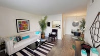 This single-floor residence offers a thoughtfully organized layout that maximizes its footprint through an efficient, open design. The living area serves as the central hub of the home, featuring rich wood-style flooring, neutral walls, and ample room for comfortable furnishings. A bold striped area rug anchors the space, complementing the clean lines of the room. A pass-through window connects the kitchen to the living and dining areas, enhancing the sense of openness and flow throughout.

The kitchen is outfitted with white cabinetry, a granite-look countertop, a stainless steel sink, and standard appliances, providing practical functionality in a compact footprint. Adjacent to the kitchen, the dedicated dining area accommodates a round table and chairs beneath a stylish pendant light fixture, creating a defined yet connected space for meals.

The bedroom offers a quieter retreat, featuring plush carpeting, a ceiling fan, and a window with natural light and outdoor views. A full bathroom serves the unit, complete with an oval vanity mirror, a single-basin sink with chrome fixtures, and a separate shower-tub area with wood-style flooring. The overall ambiance throughout is bright, clean, and cohesive.